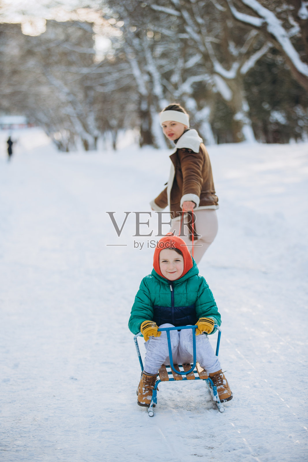 妈妈在冬季公园里拉着儿子滑雪橇,享受着冬日的乐趣照片摄影图片