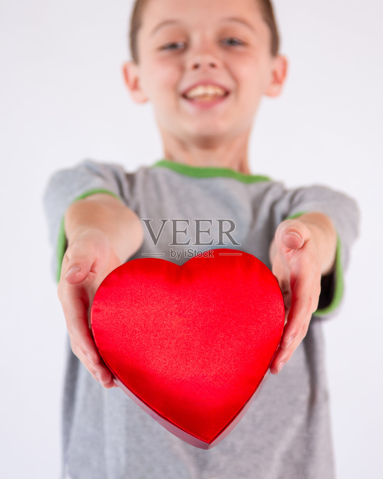 男孩张开双臂,手中拿着心形红色盒子,摄影棚内照片摄影图片