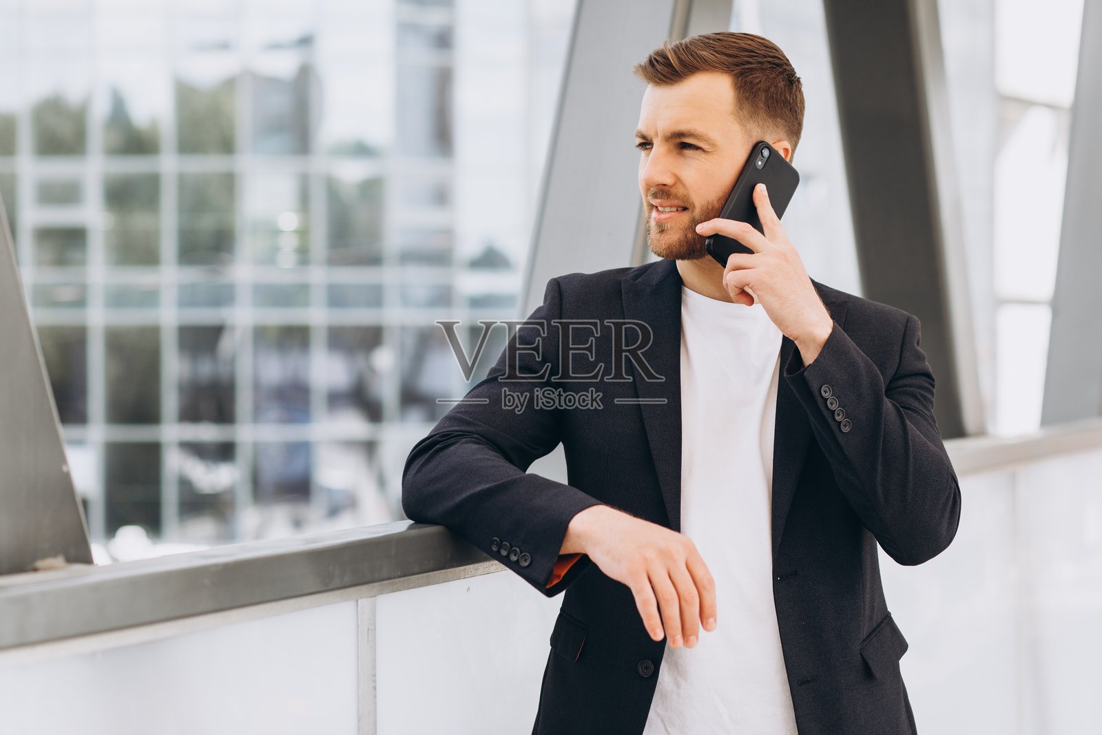 年轻的成年商人正在未来感的背景下,倚靠着栏杆,若有所思地讲着电话。照片摄影图片