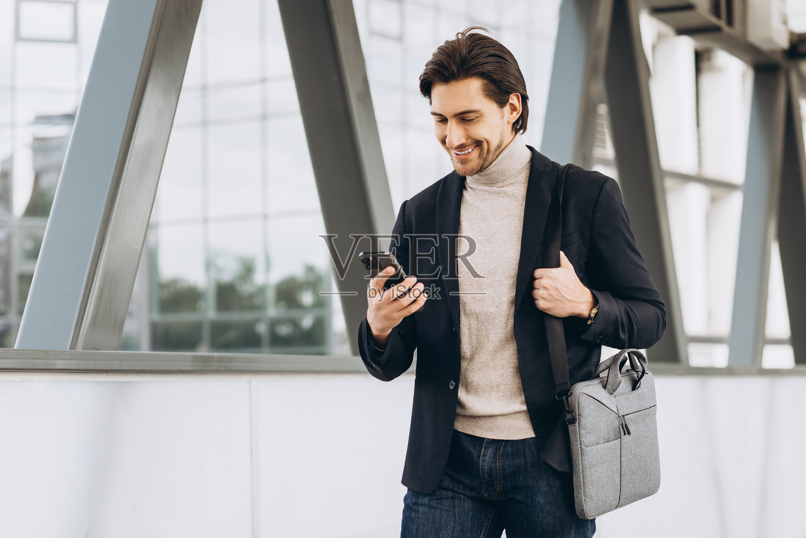 一位职业商人微笑着在通勤途中走在现代都市中,同时查看着智能手机照片摄影图片