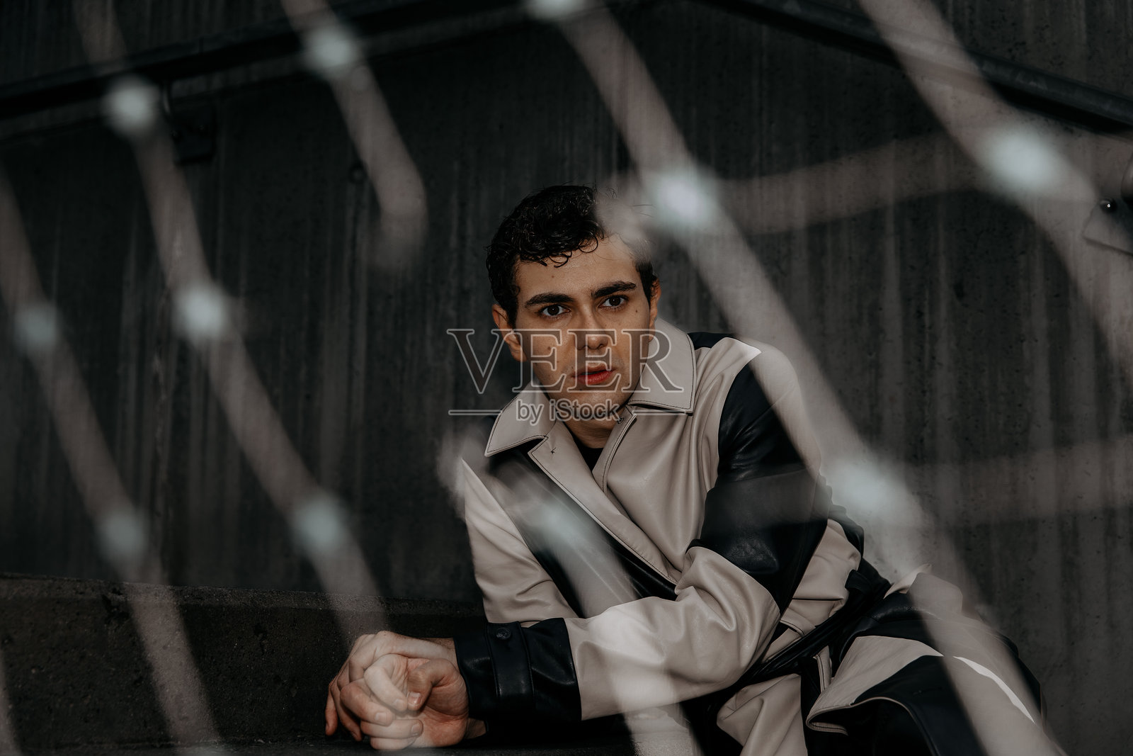 穿着时尚风衣的年轻高加索男性,站在栅栏后面照片摄影图片