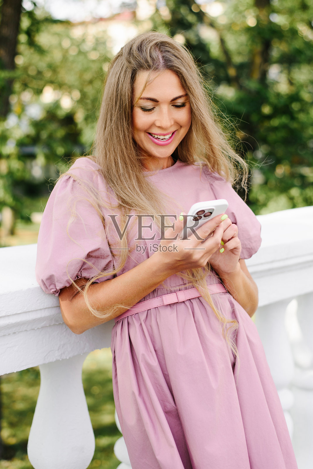 一位女士在户外对着智能手机发短信,脸上带着笑容照片摄影图片