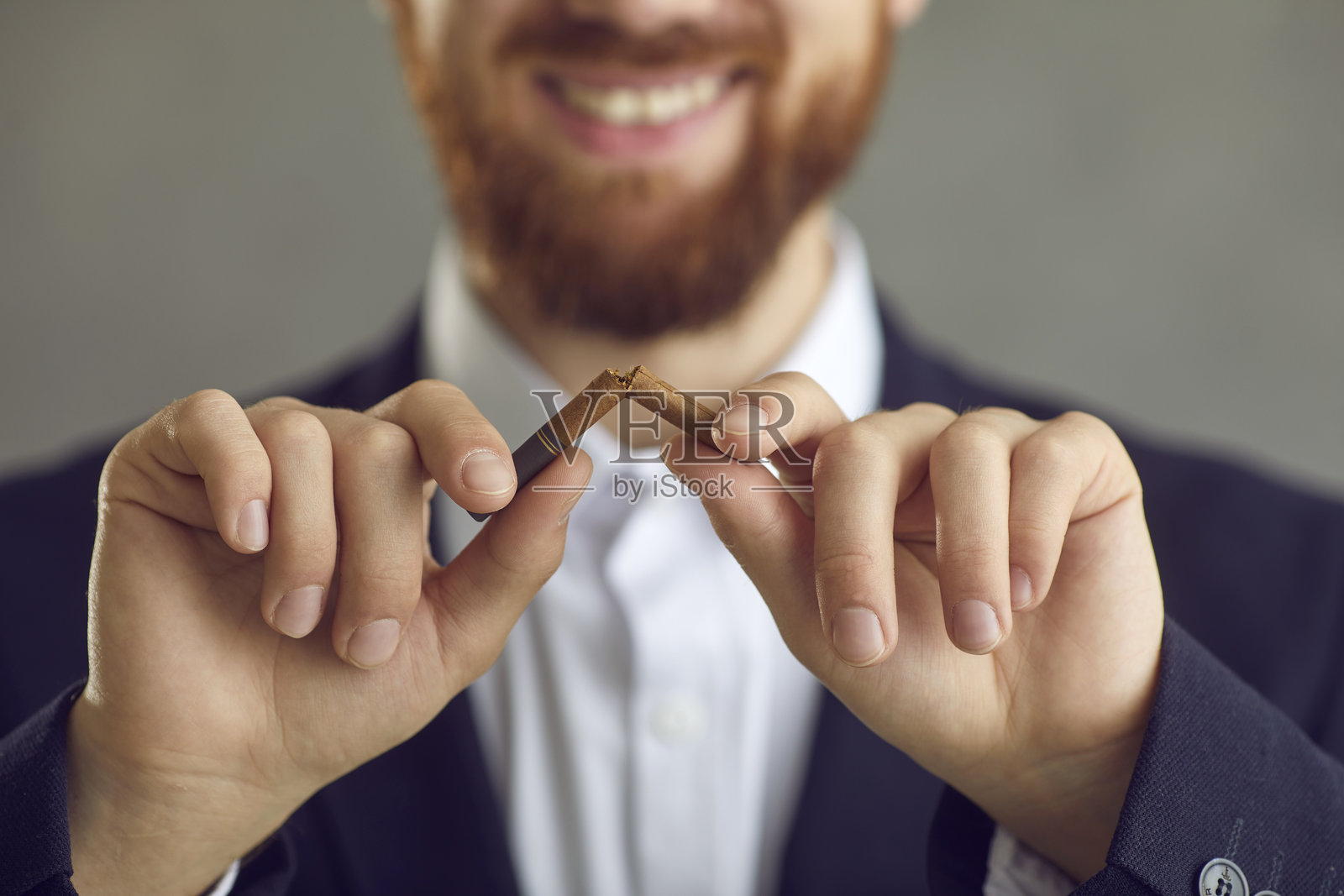 微笑的高加索男性正在折断香烟,背景为灰色留白区域照片摄影图片