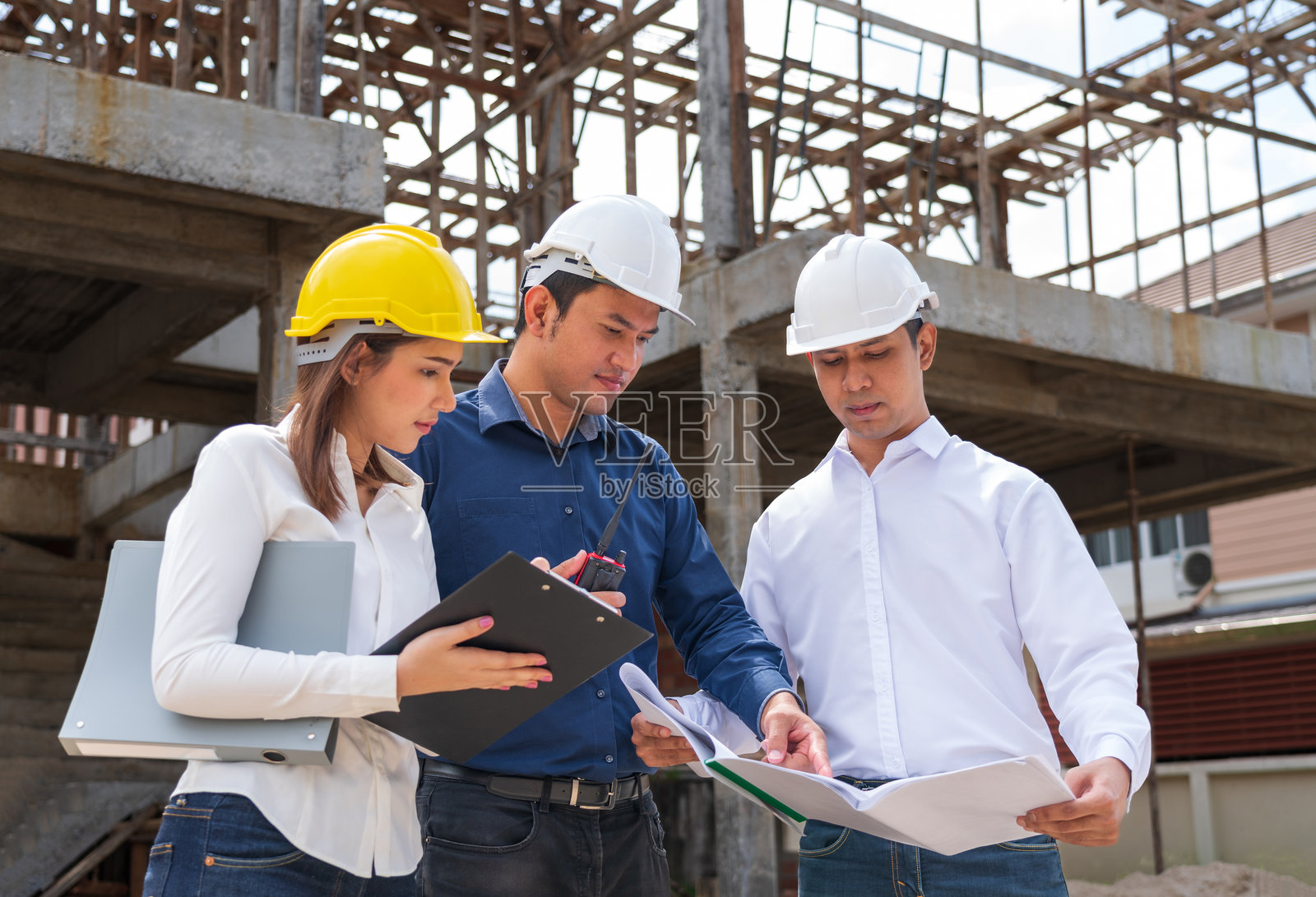 工程师团队与工人开会,讨论带有建筑蓝图的现场工作,并指向工作场所。戴着安全帽的建筑工人和建筑师在建筑工地上查看蓝图。照片摄影图片