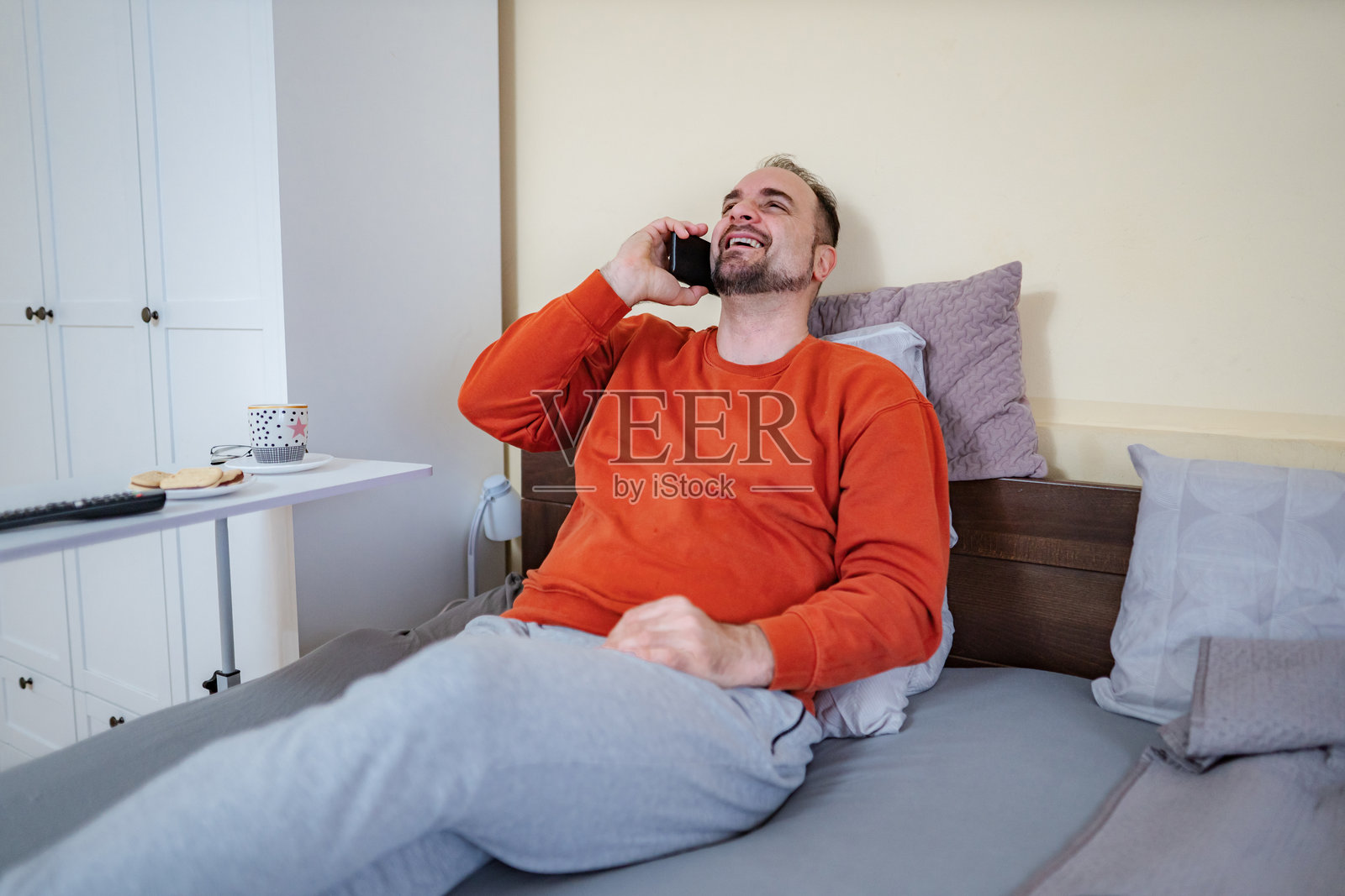 男人在床上边打电话边笑着照片摄影图片