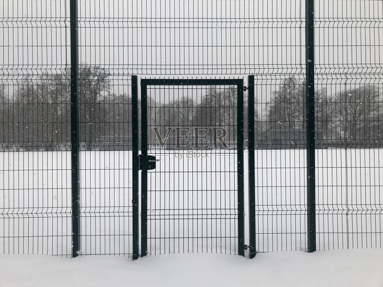 高高的金属栅栏后是一片被雪覆盖的田野,栅栏门紧闭着照片摄影图片