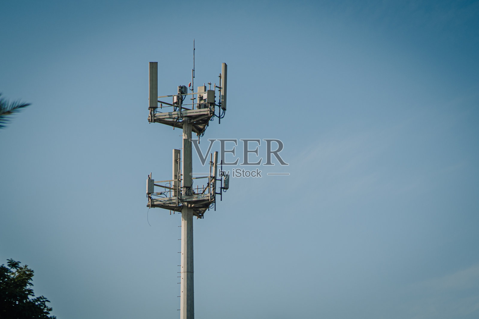 蓝天下的电信塔,配有天线和设备,周围环绕着树木,展示着城市环境中的现代通信基础设施照片摄影图片