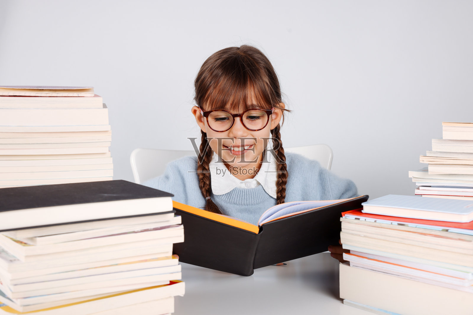 留着金色辫子的小学生女孩,面带微笑,身旁放着叠起来的书籍照片摄影图片