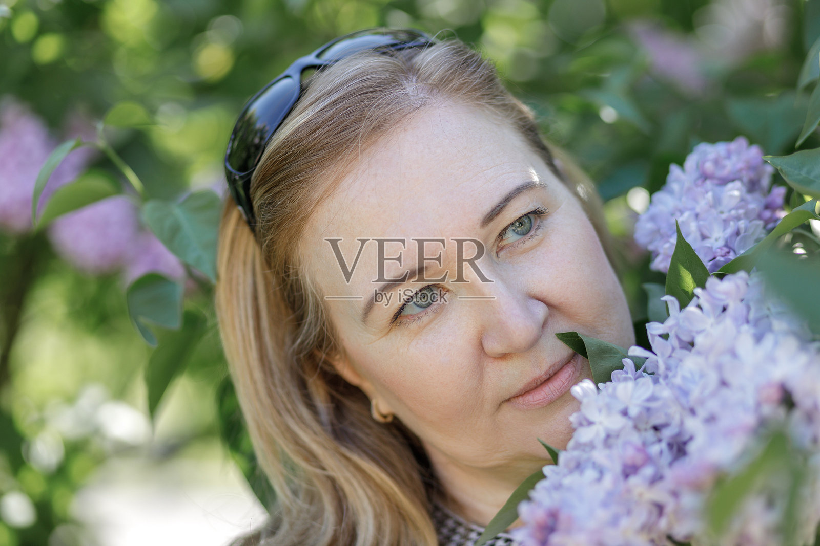 一位金发女子站在城市公园盛开的丁香花旁。夏季。照片摄影图片
