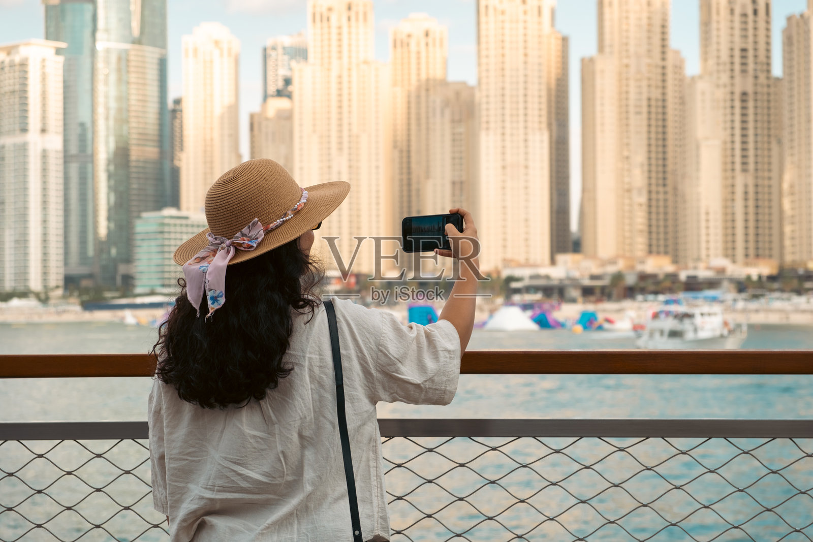 戴着帽子的女士在海滩上拍摄迪拜码头照片摄影图片