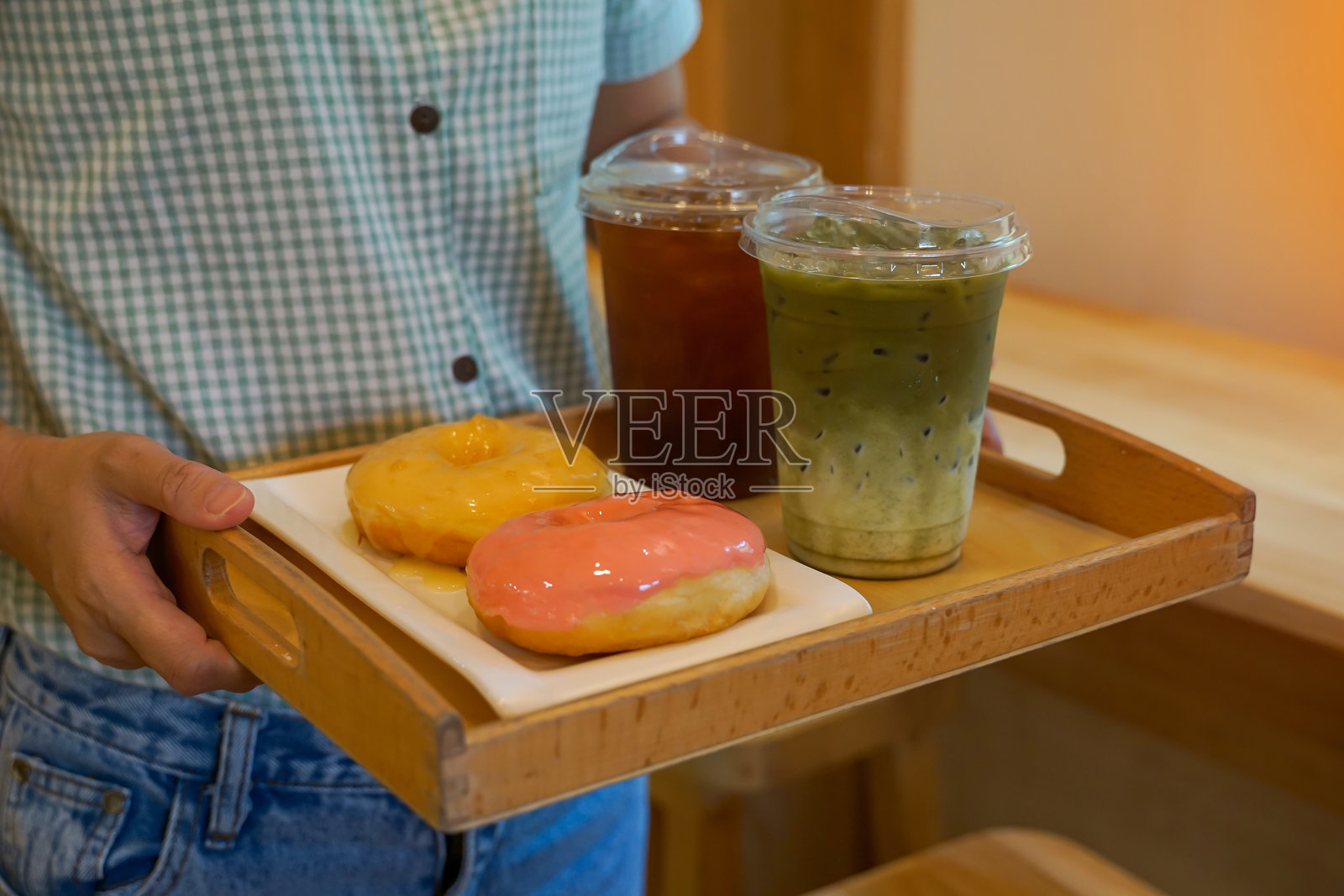 一位服务员在现代咖啡馆为顾客提供清爽的冰饮和美味的草莓奶油甜甜圈。体现了餐饮服务、甜点和下午茶的概念。照片摄影图片