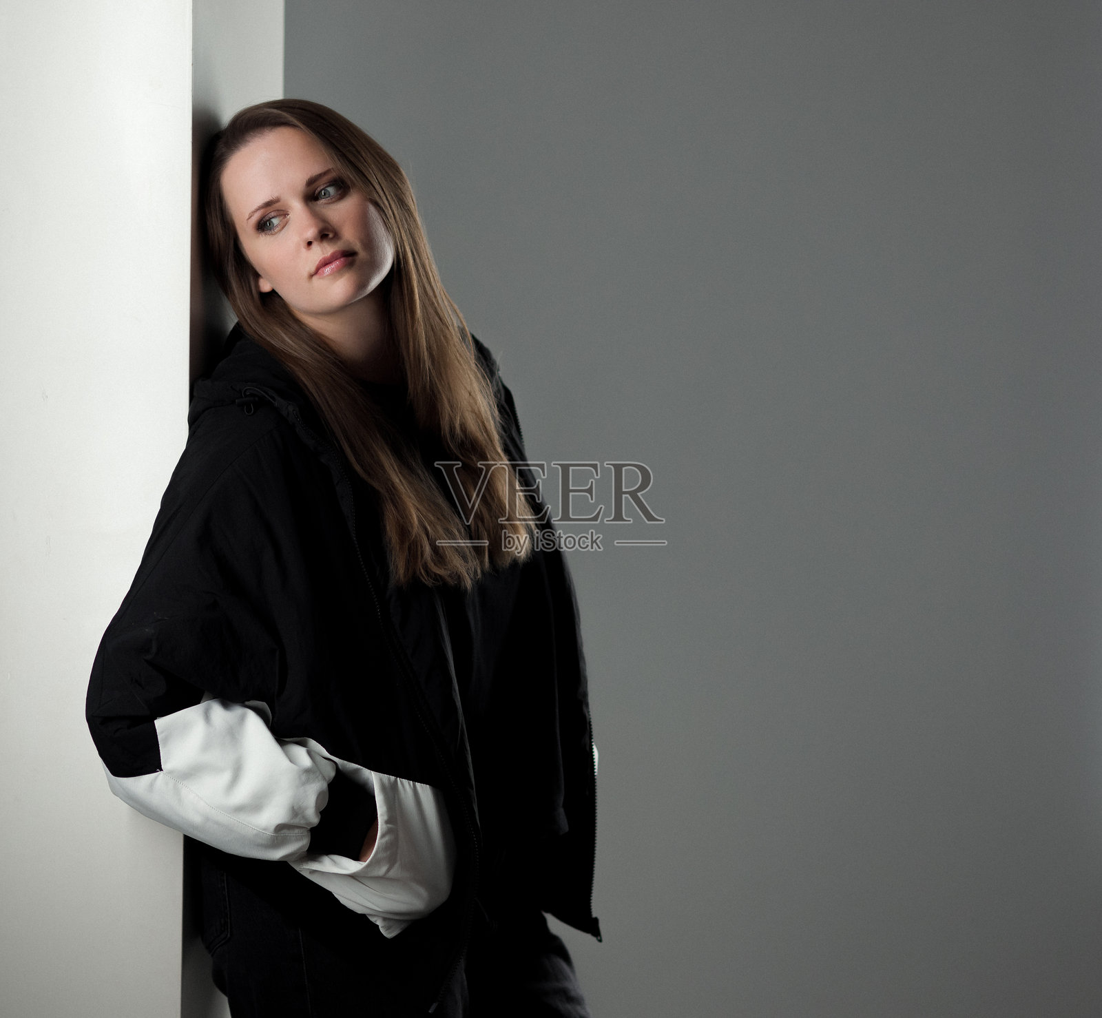 年轻女子倚靠墙壁,望向别处,若有所思地摆姿势照片摄影图片