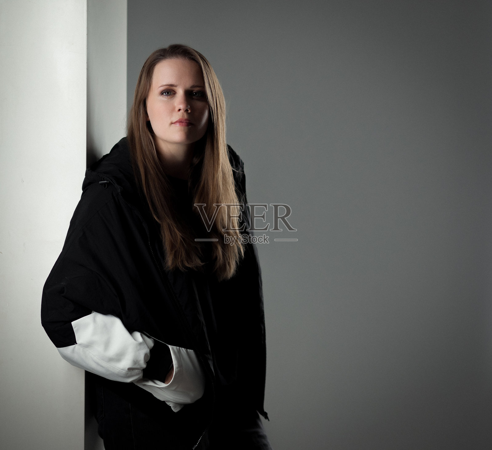 年轻女子倚靠墙壁,身穿黑白外套照片摄影图片