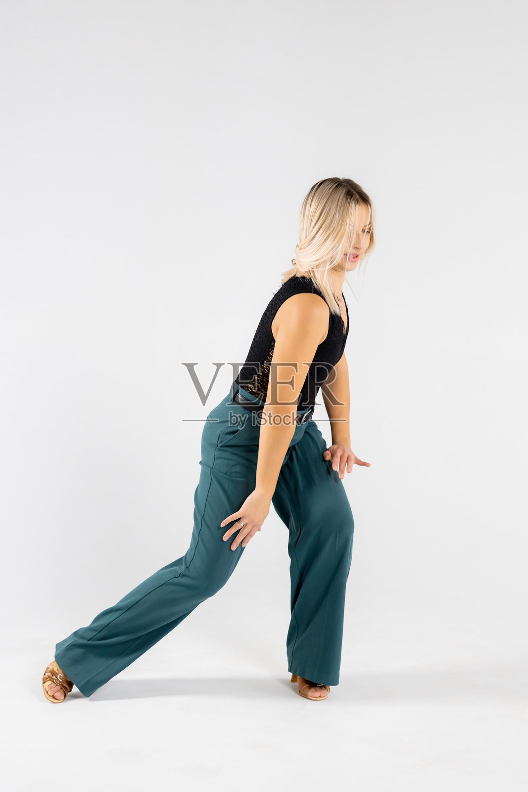 一位金发年轻舞者双手合十、双腿分开,在白色背景前摆出姿势照片摄影图片