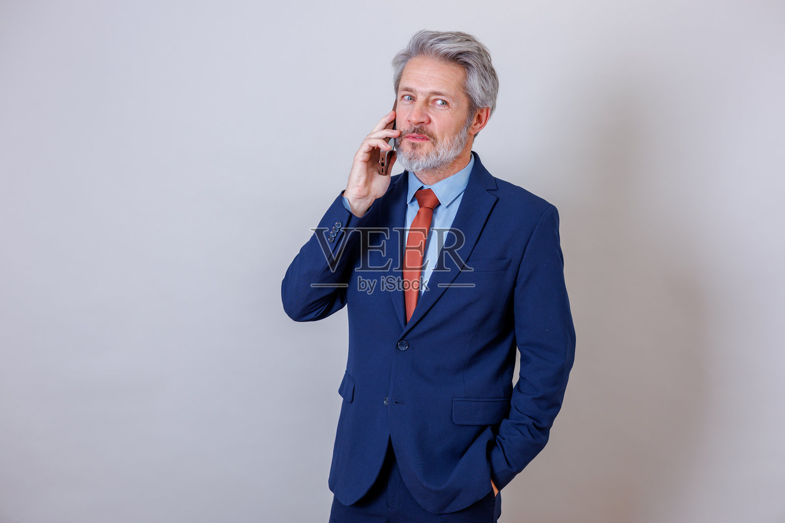 身着蓝色西装、系着红色领带的专业商务人士正在对着镜头接听智能手机并进行沟通。照片摄影图片