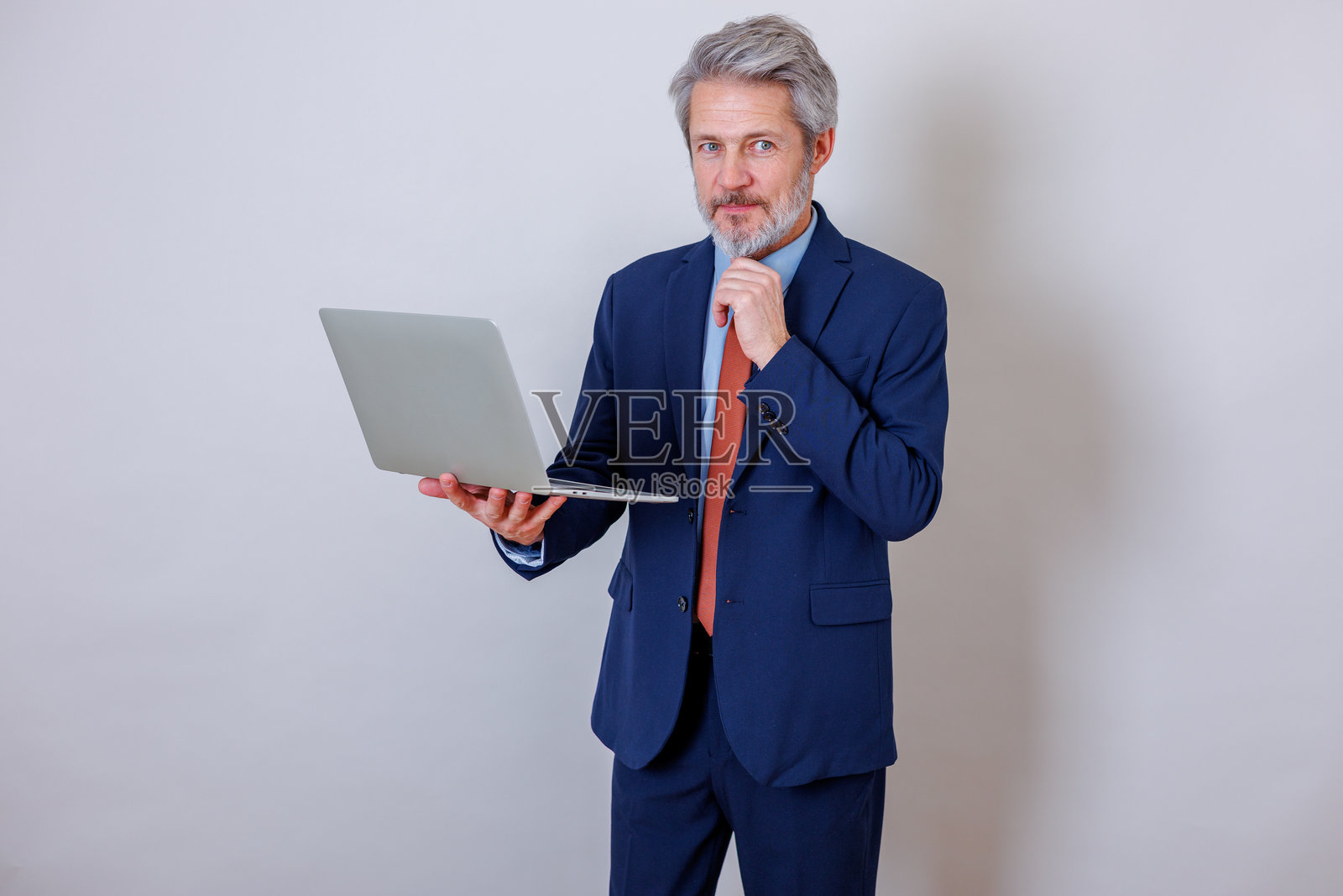 一位穿着蓝色西装的成熟商人,手持笔记本电脑,正在为他的企业业务思考新的想法和解决方案。照片摄影图片