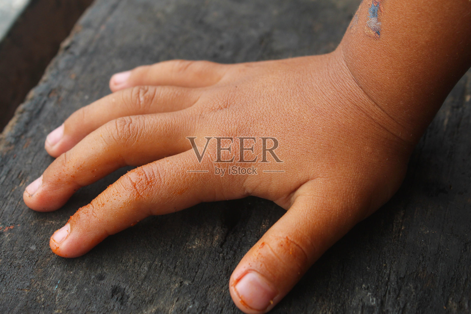 孩子弄脏的手沾染了食物残渣或辛辣香料,出现在深色木质表面上照片摄影图片