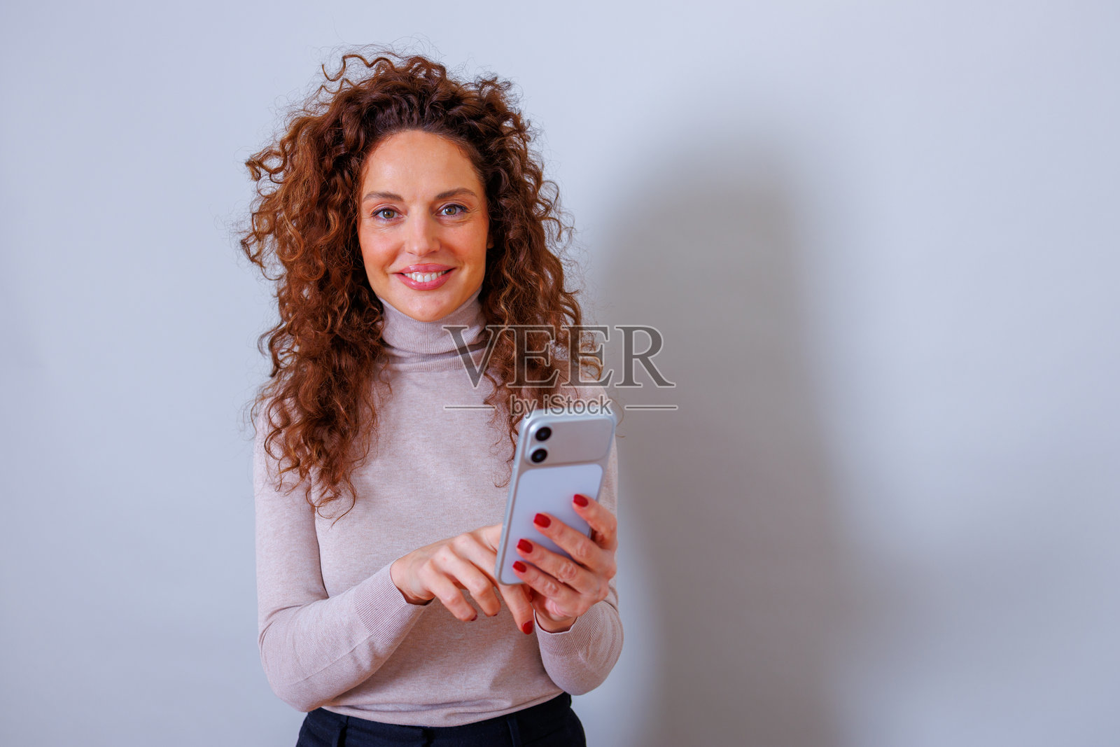 卷发女子微笑着轻触智能手机,与人连接并浏览网络照片摄影图片