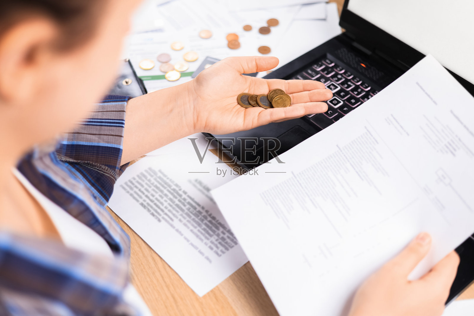 一位女士拿着欧元硬币,在笔记本电脑旁查看纸币。家庭预算和财务规划的概念:金钱和文件放在桌子上。照片摄影图片