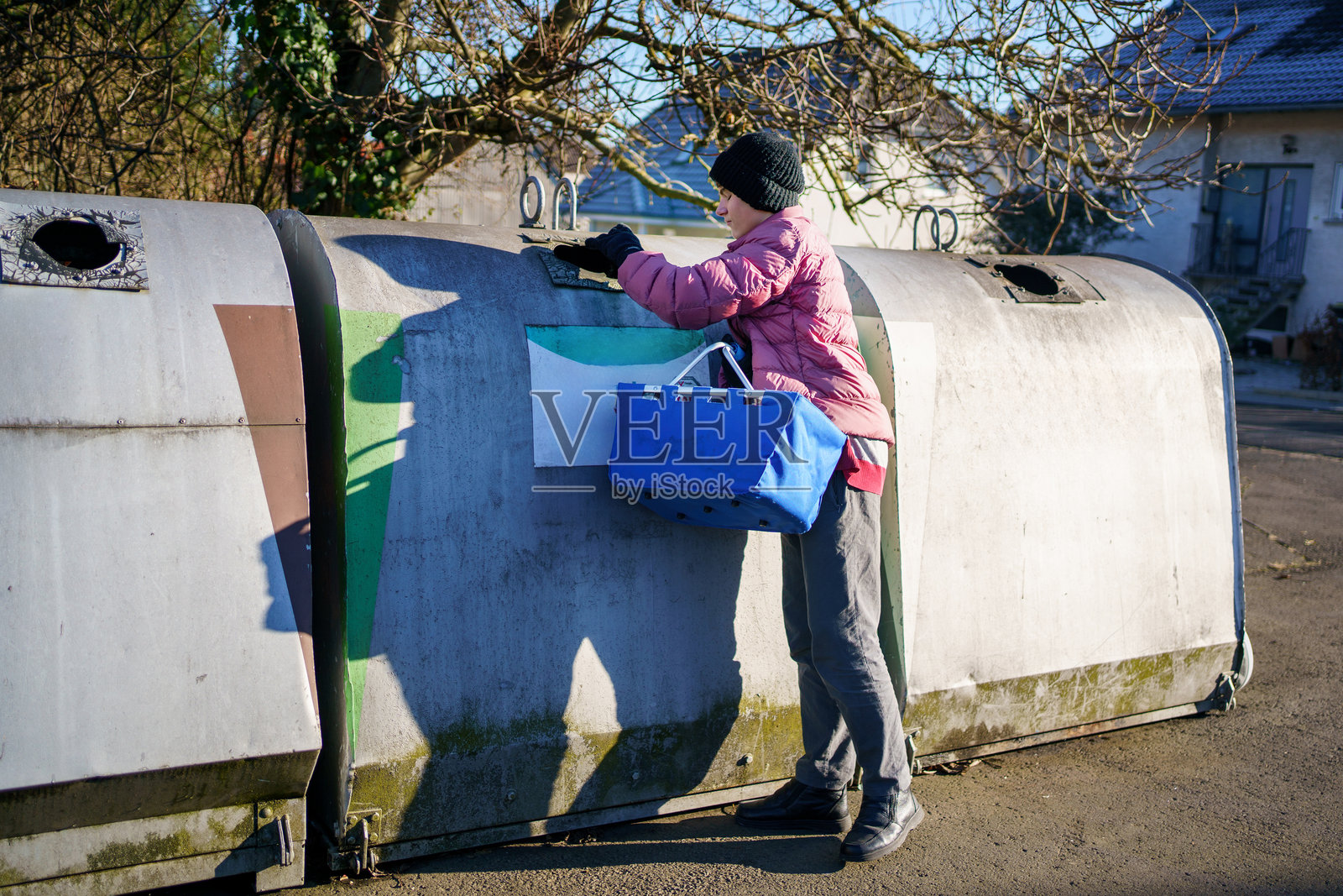 十几岁的男孩正在将空瓶子扔进垃圾箱。他正在帮忙做家务。照片摄影图片