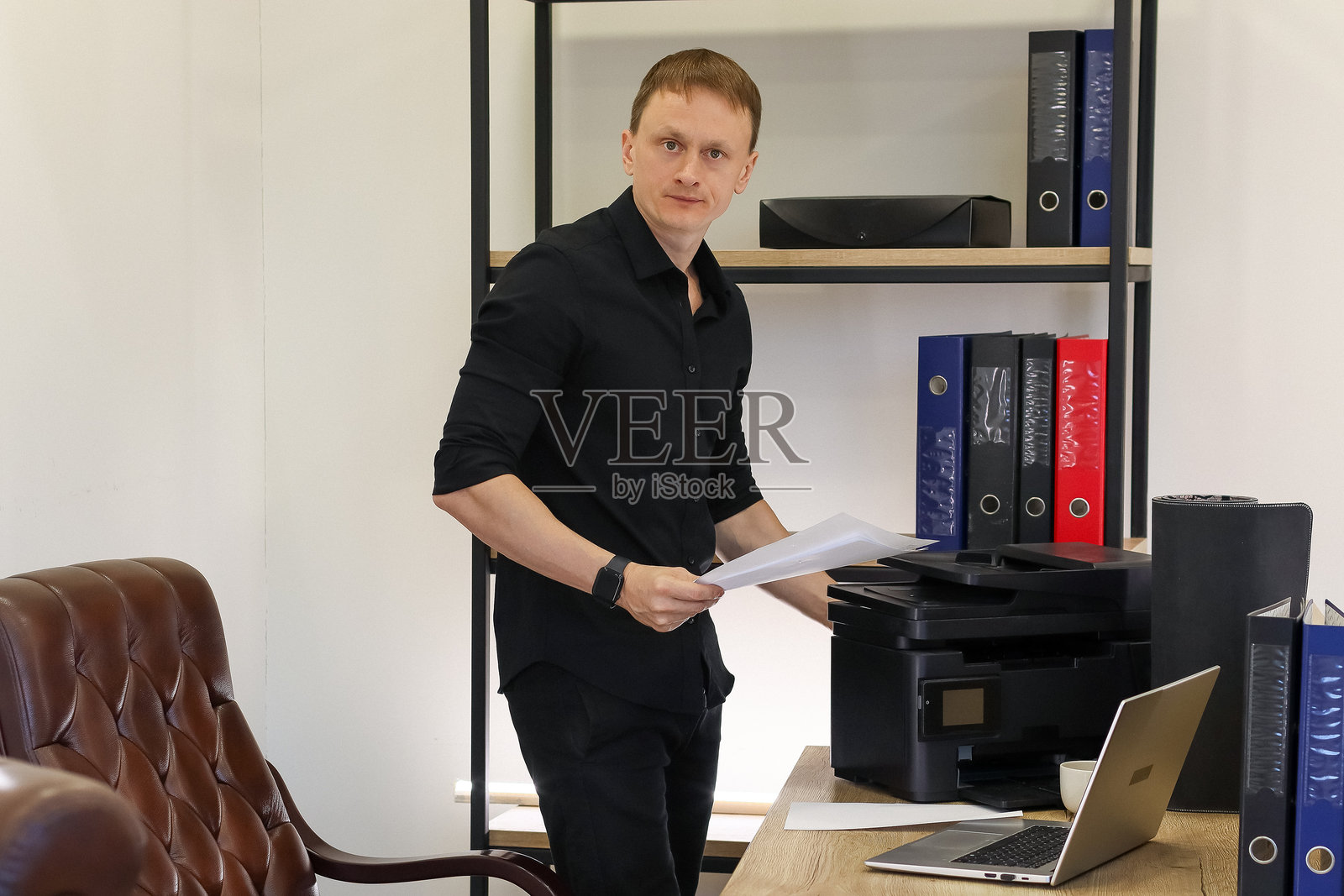 商人拿着打印好的纸张在办公室打印机旁照片摄影图片