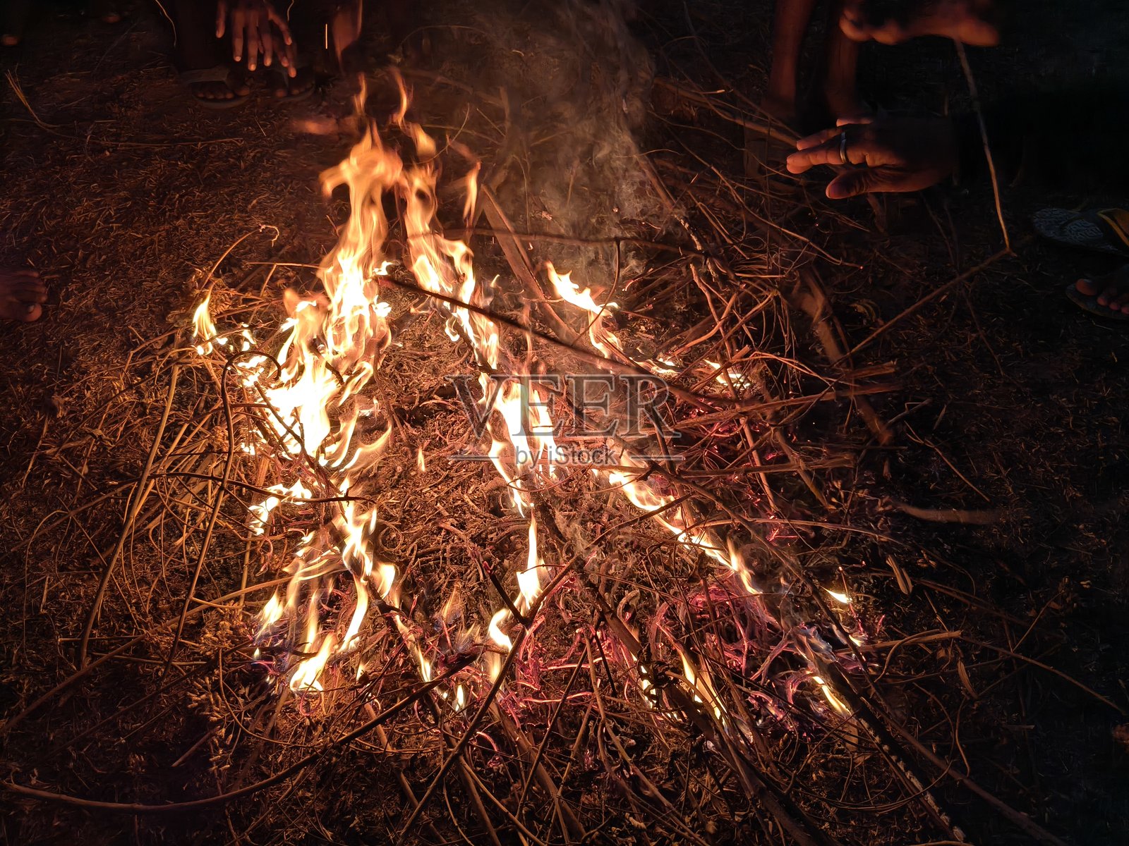 人们围坐在篝火旁,暖着手和脚。照片摄影图片