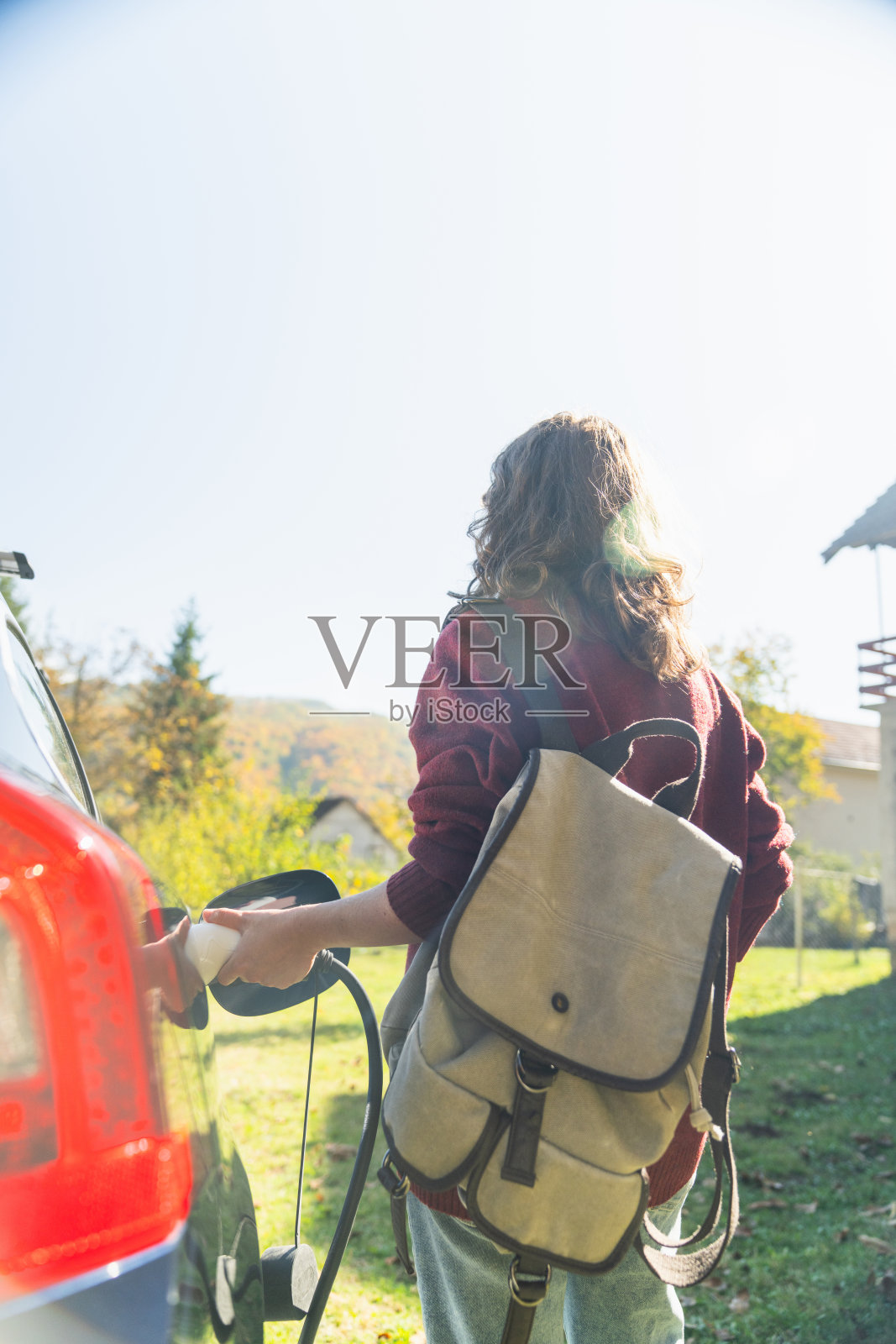 背着背包的女性旅行者站在充电的电动汽车旁边照片摄影图片