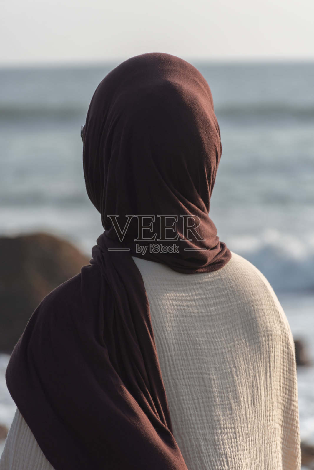 一位戴着头巾的女性站在海边,若有所思地凝视着海平线照片摄影图片