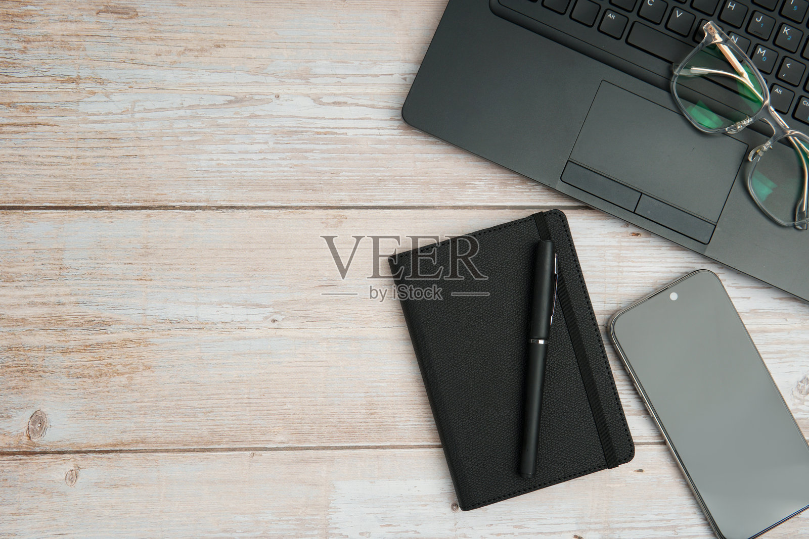 俯视视角下的商务工作空间,白色木质桌面上摆放着笔记本电脑、眼镜、笔记本和智能手机,展现了高效、数字工作、规划和专业的办公室设置,并留有干净的复制空间。照片摄影图片