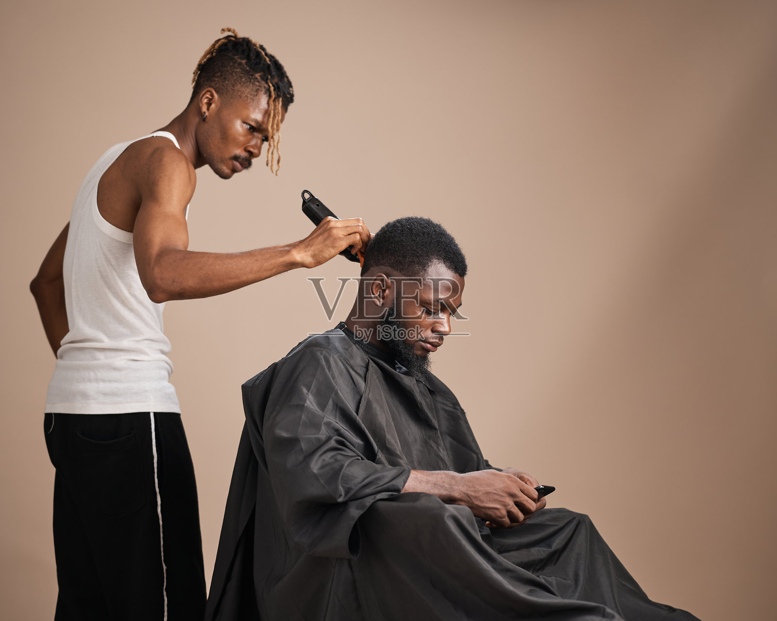 年轻的黑人理发师在工作室里为坐着的顾客修剪头发照片摄影图片