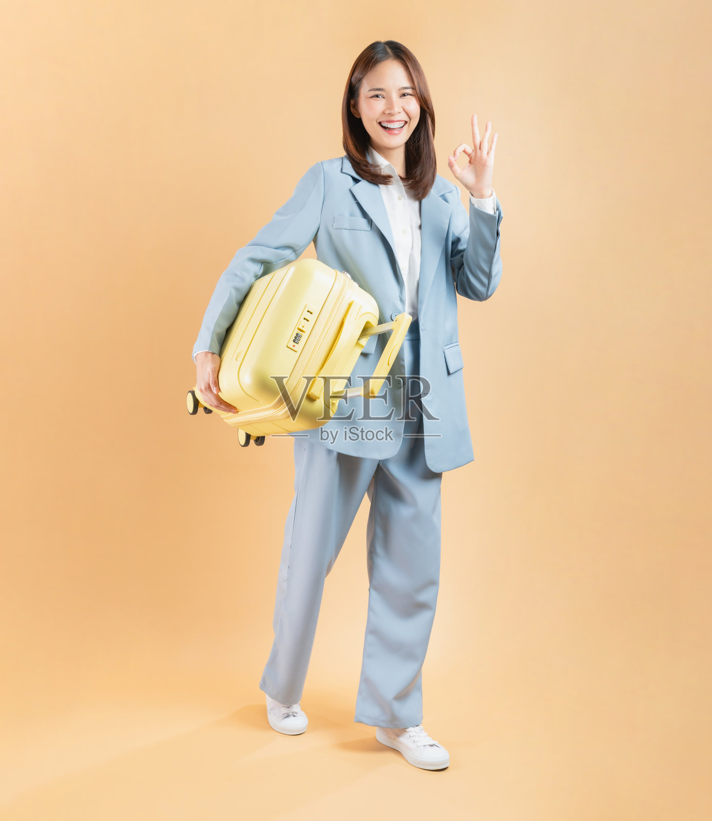 快乐的亚洲女商人,手持行李箱,孤立在米色背景上,旅行概念。照片摄影图片