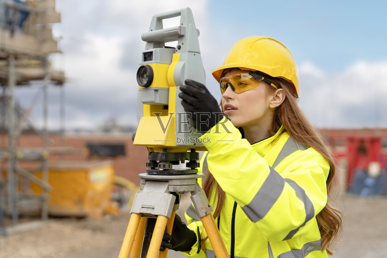 身穿鲜艳反光安全装备的女建筑测量员在建筑工地上使用测量设备照片摄影图片