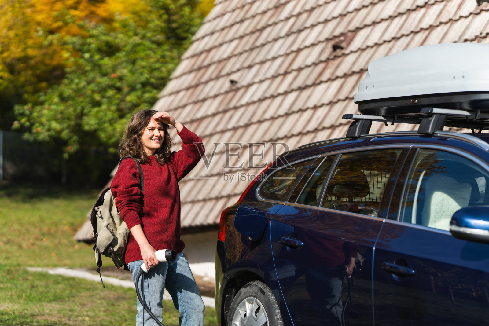 背着背包的女性旅行者,站在一辆正在充电的电动车旁边照片摄影图片