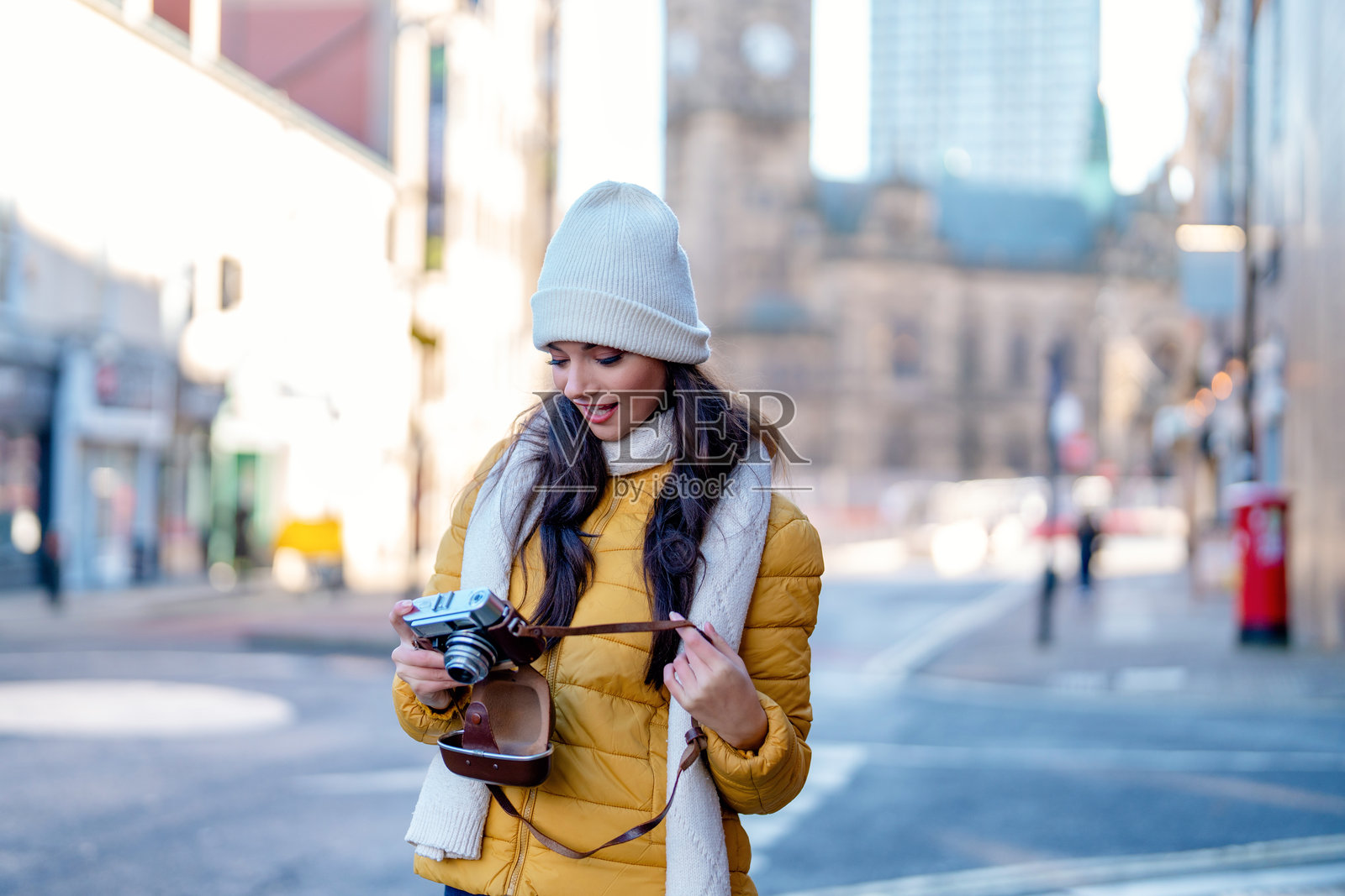一位女士穿着夹克和冬季帽子,在城市街道上拿着相机照片摄影图片