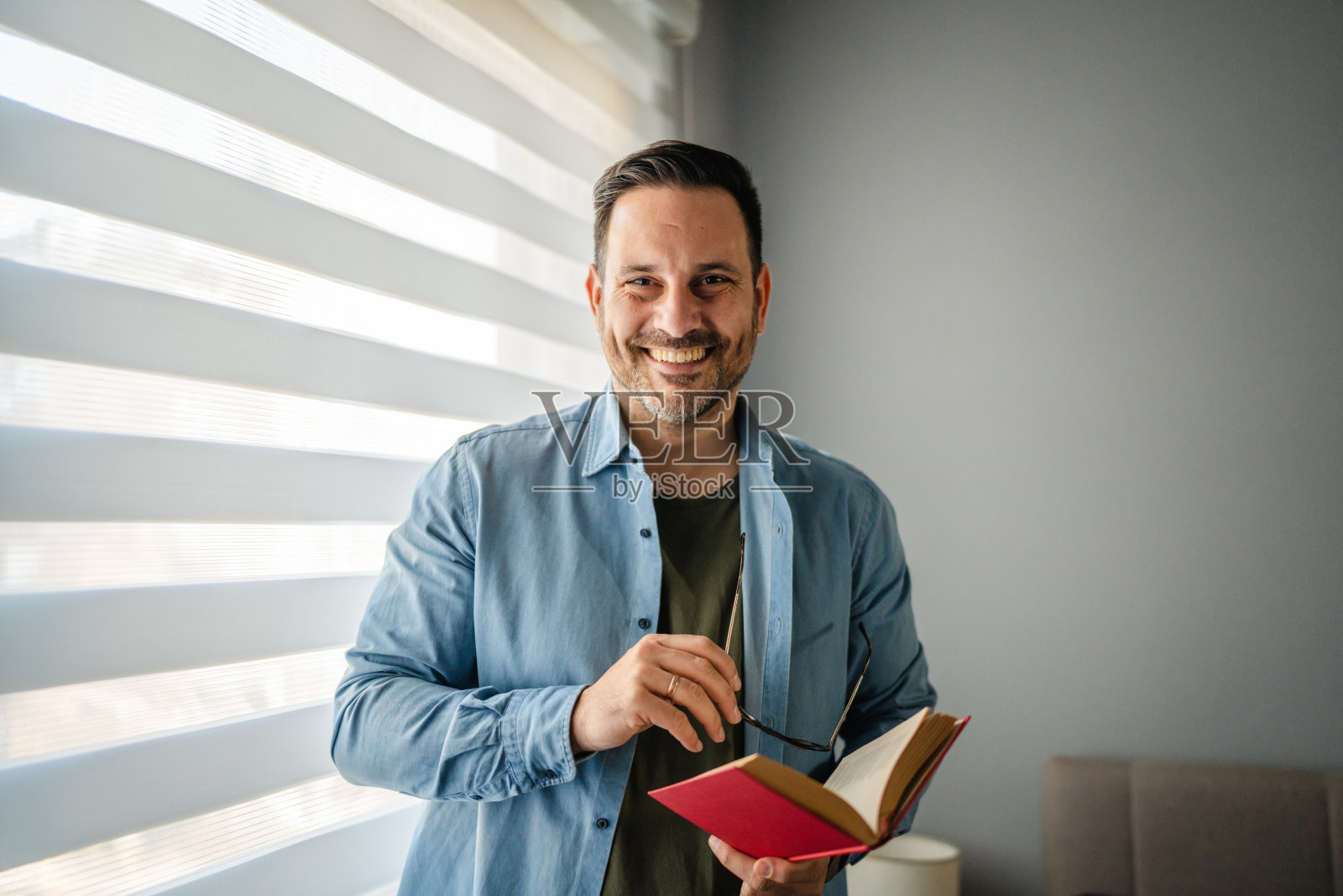 窗边,一位戴着眼镜的男士微笑着手持一本书照片摄影图片