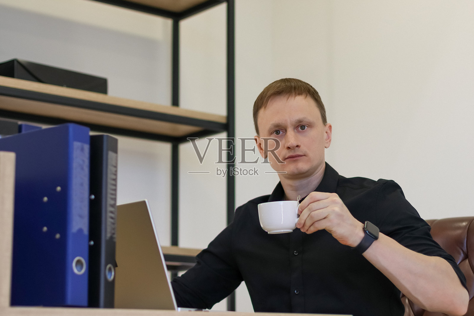职业男性在办公桌前,面对着打开的电脑,若有所思地举起咖啡杯。照片摄影图片