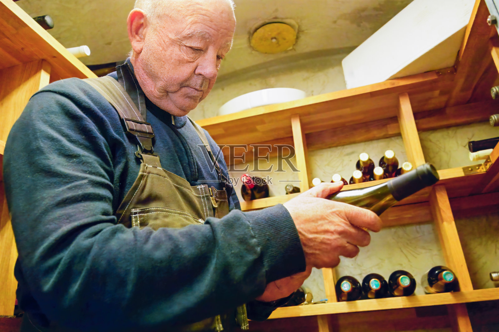 一位年长男子在酒窖里检查酒瓶。照片摄影图片