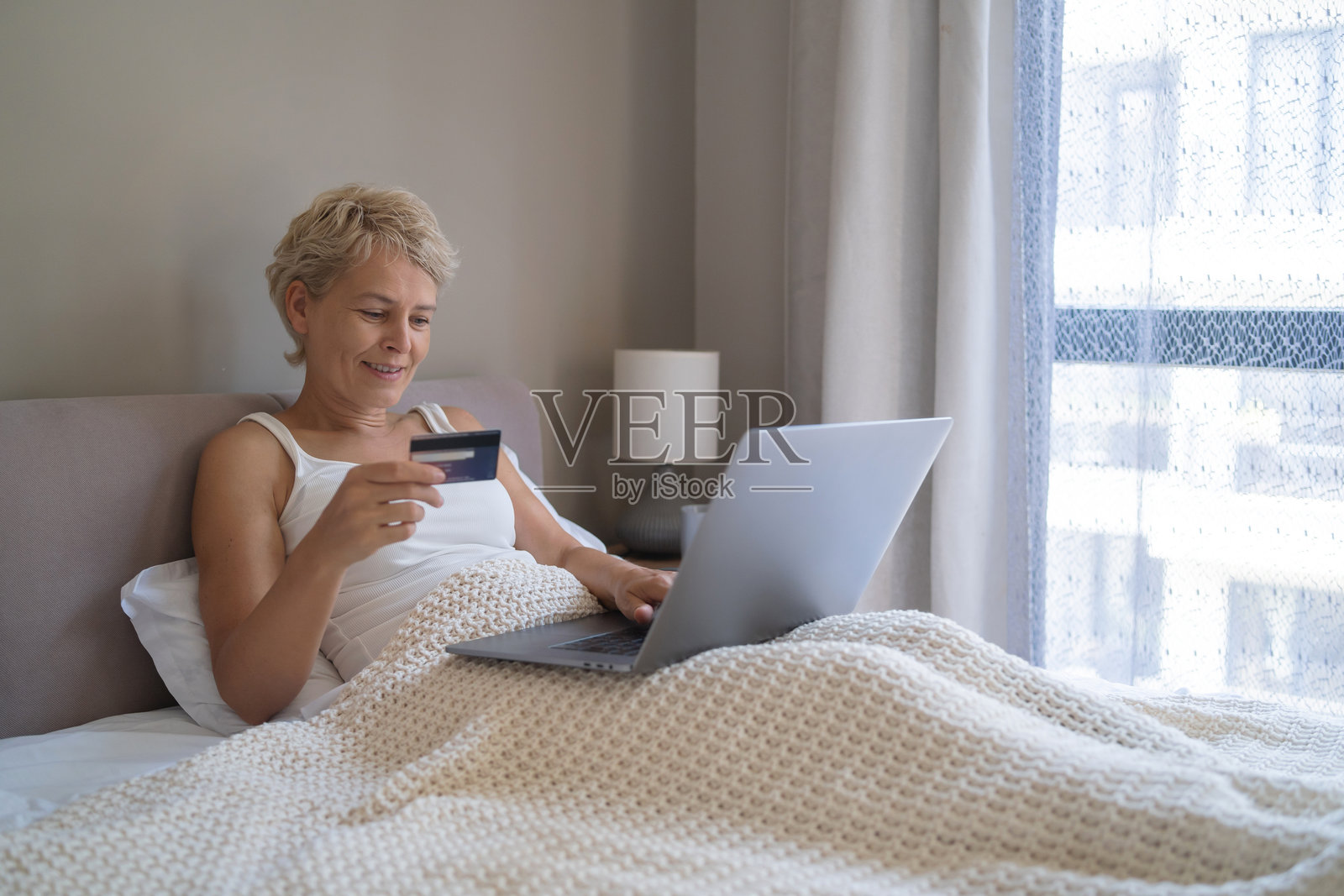 女子在床上用笔记本电脑和信用卡在线购物照片摄影图片