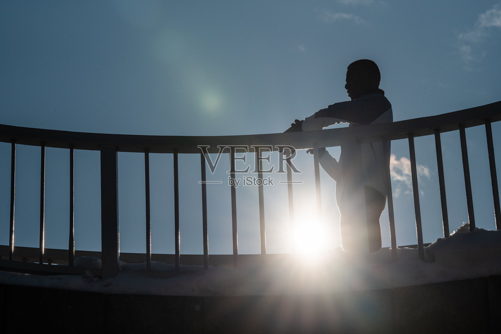 冬季阳光下,一个人影靠在栏杆上休息照片摄影图片