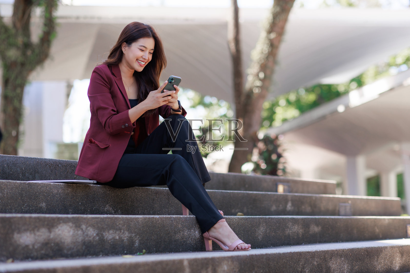 亚洲女性坐在台阶上,面带微笑地使用智能手机照片摄影图片