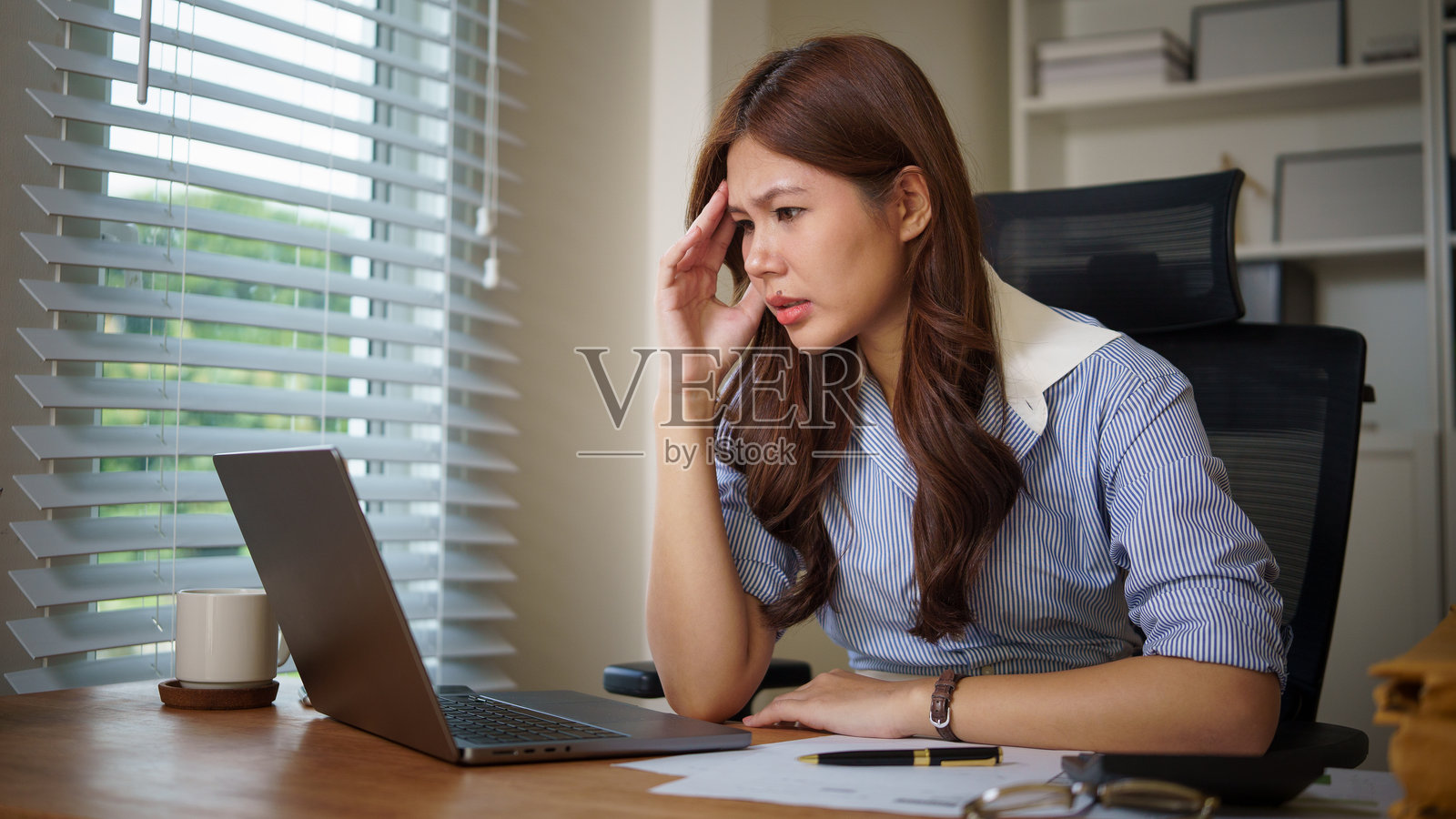 过劳的女商人专注于笔记本电脑,象征着工作中的压力、截止日期和职业倦怠。照片摄影图片