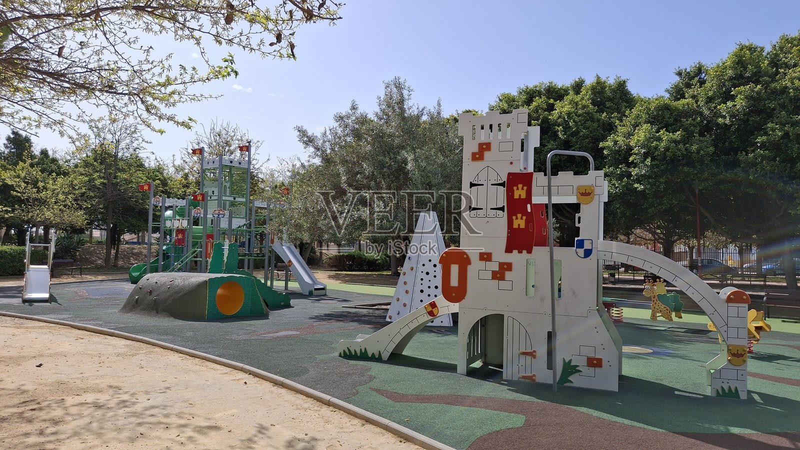 晴朗的蓝天下,地中海的阳光午后,公园里有儿童游乐场,四周环绕着高大的树木。照片摄影图片