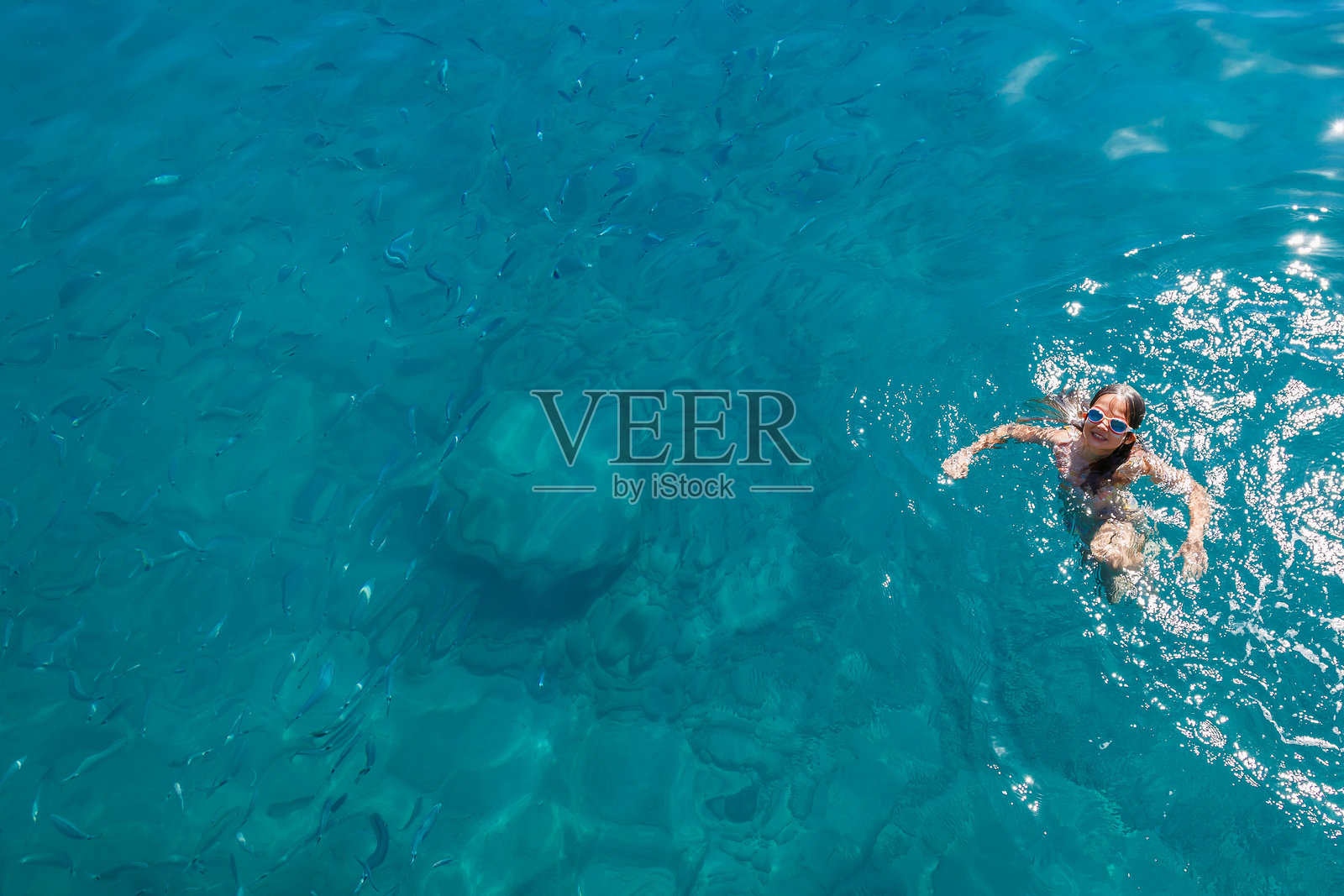 快乐的年轻女孩在清澈碧绿的海水中与鱼群一同游泳,展现了暑期度假和浮潜探险的概念照片摄影图片