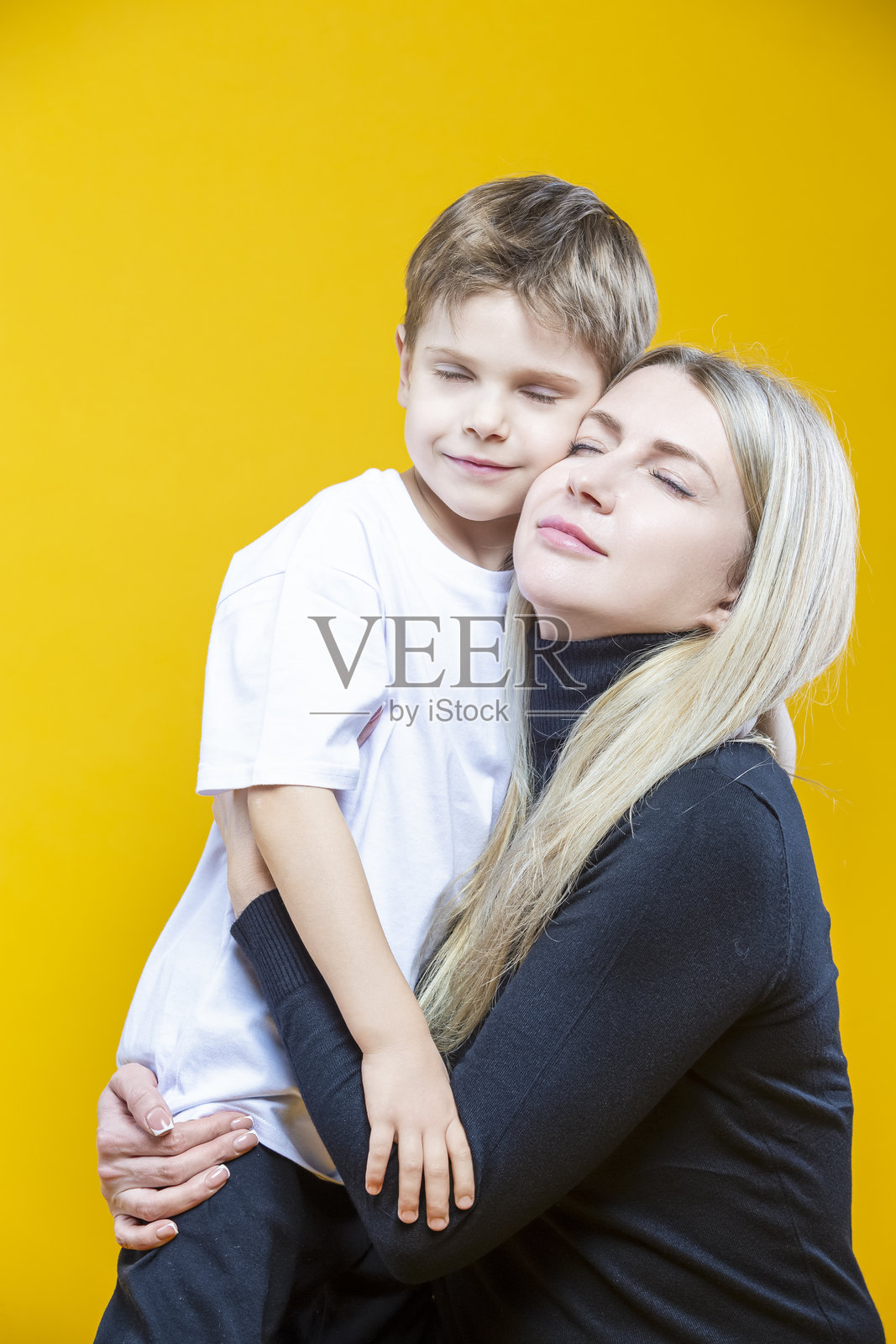 快乐的夫妇,女人和孩子,穿着休闲服,妈妈和小儿子拥抱依偎,竖幅图像,在黄色背景上摆姿势照片摄影图片