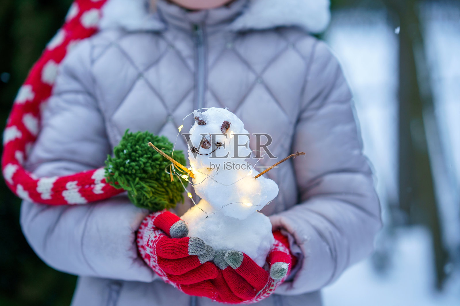 下雪天,一个穿着冬装的孩子在户外抱着一个发光的小手工雪人,温馨的季节性的生活瞬间。照片摄影图片