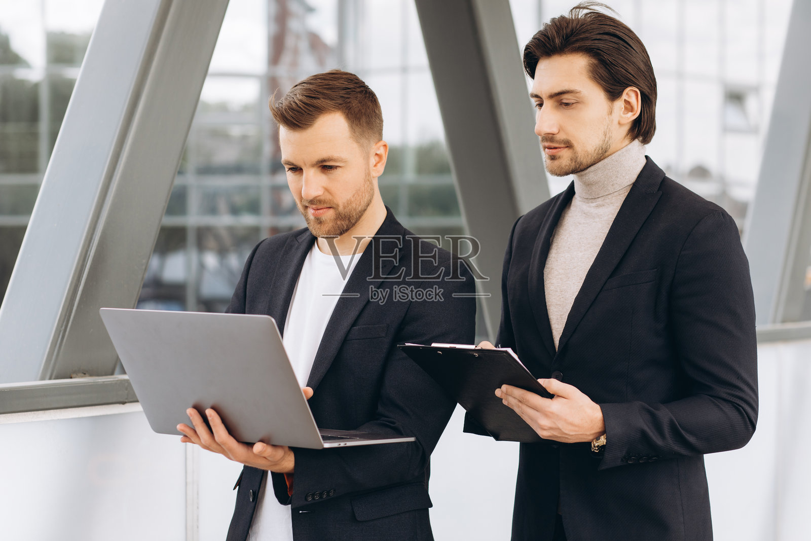 商界人士在笔记本电脑上协作,讨论项目,站在现代企业环境的户外照片摄影图片