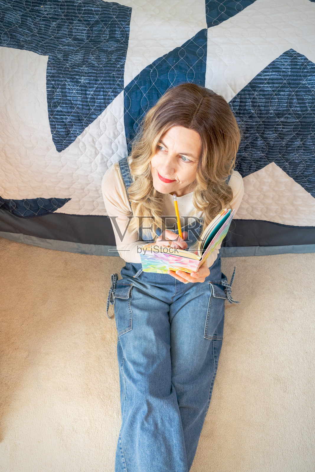 中年女性坐在卧室地板上,手持日记本,若有所思照片摄影图片