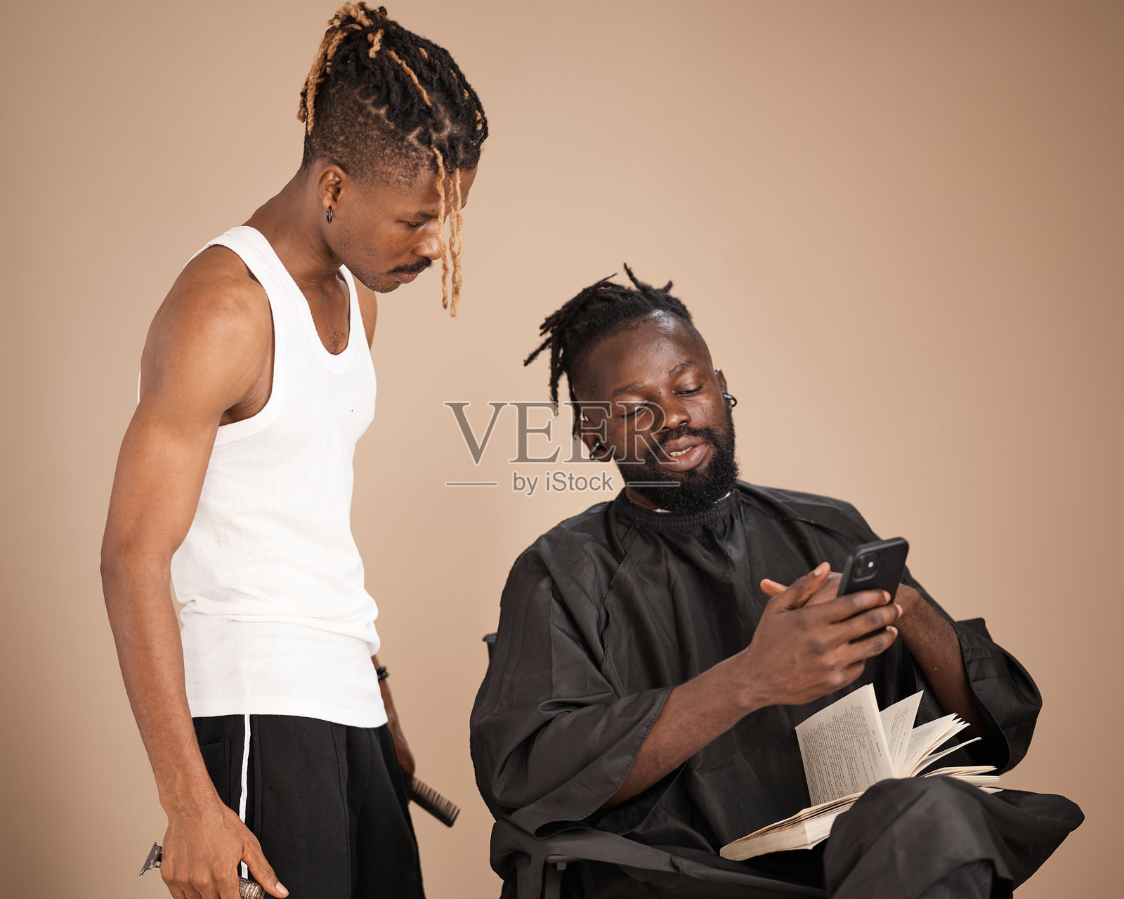 年轻的黑人理发师在理发时给坐着的顾客看手机照片摄影图片