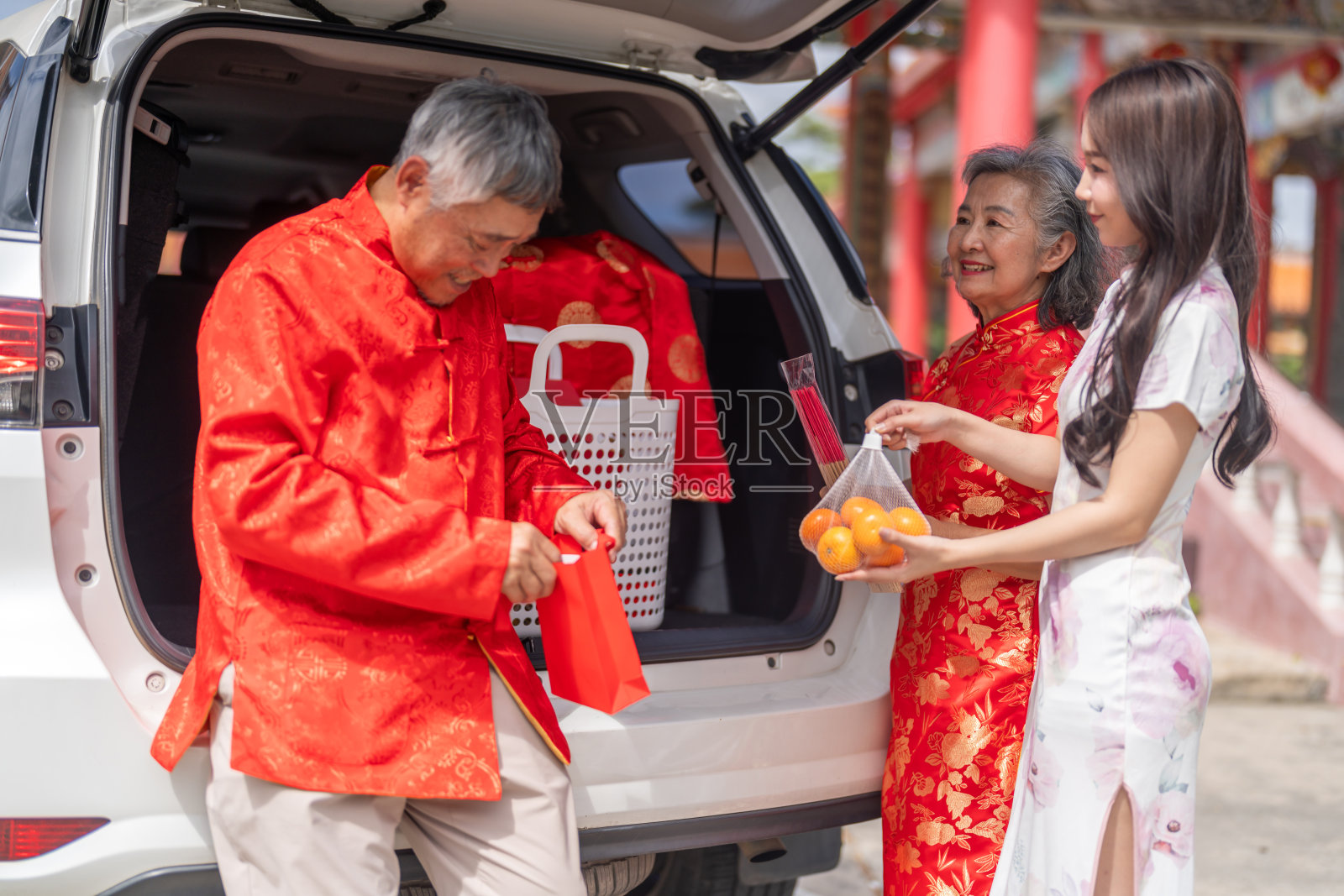 春节期间,幸福的亚裔家庭在后备箱旁为旅行做准备,年迈的父母和女儿正在将礼物装上白色汽车,公路旅行、节日返乡和交通概念照片摄影图片