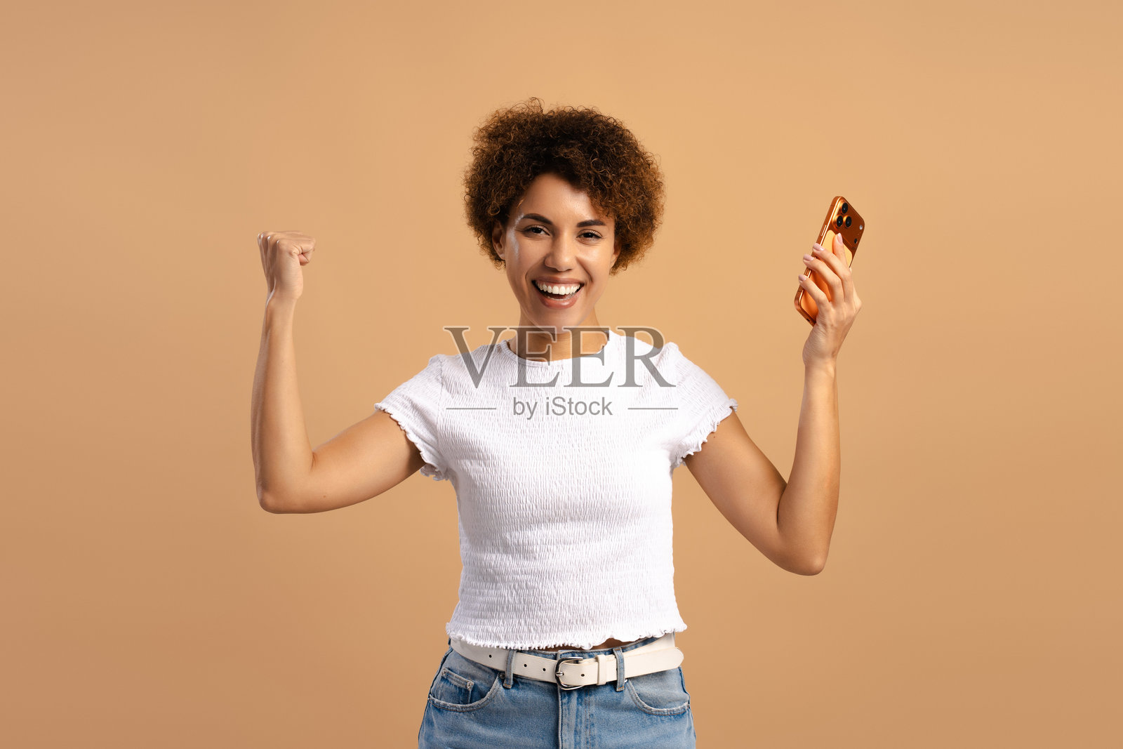 一名兴奋的非裔美国女性在米色背景上庆祝在线成功,赢得金钱照片摄影图片